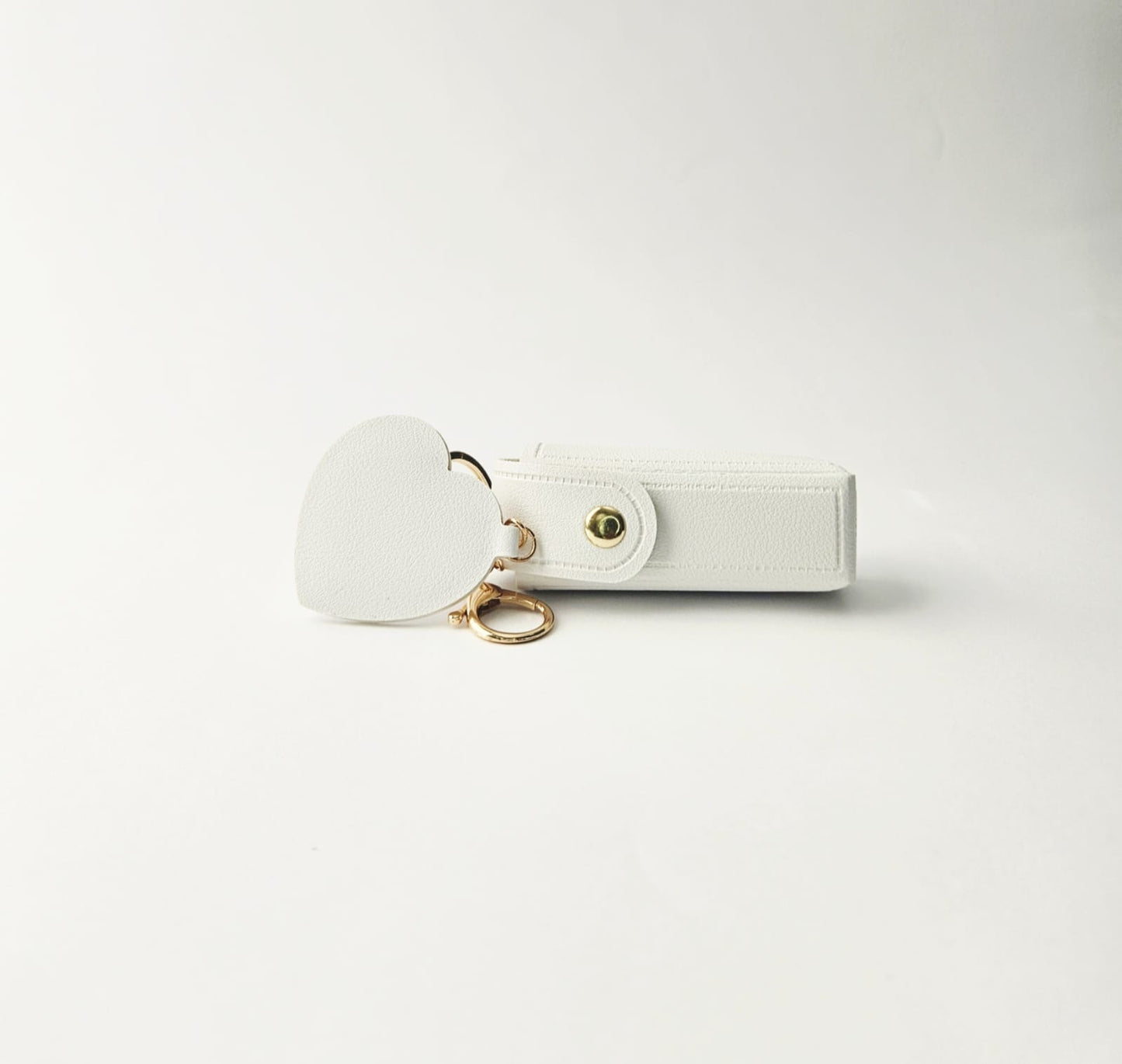 White keychain with a lipstick holder and heart shaped mirror on a light gray background