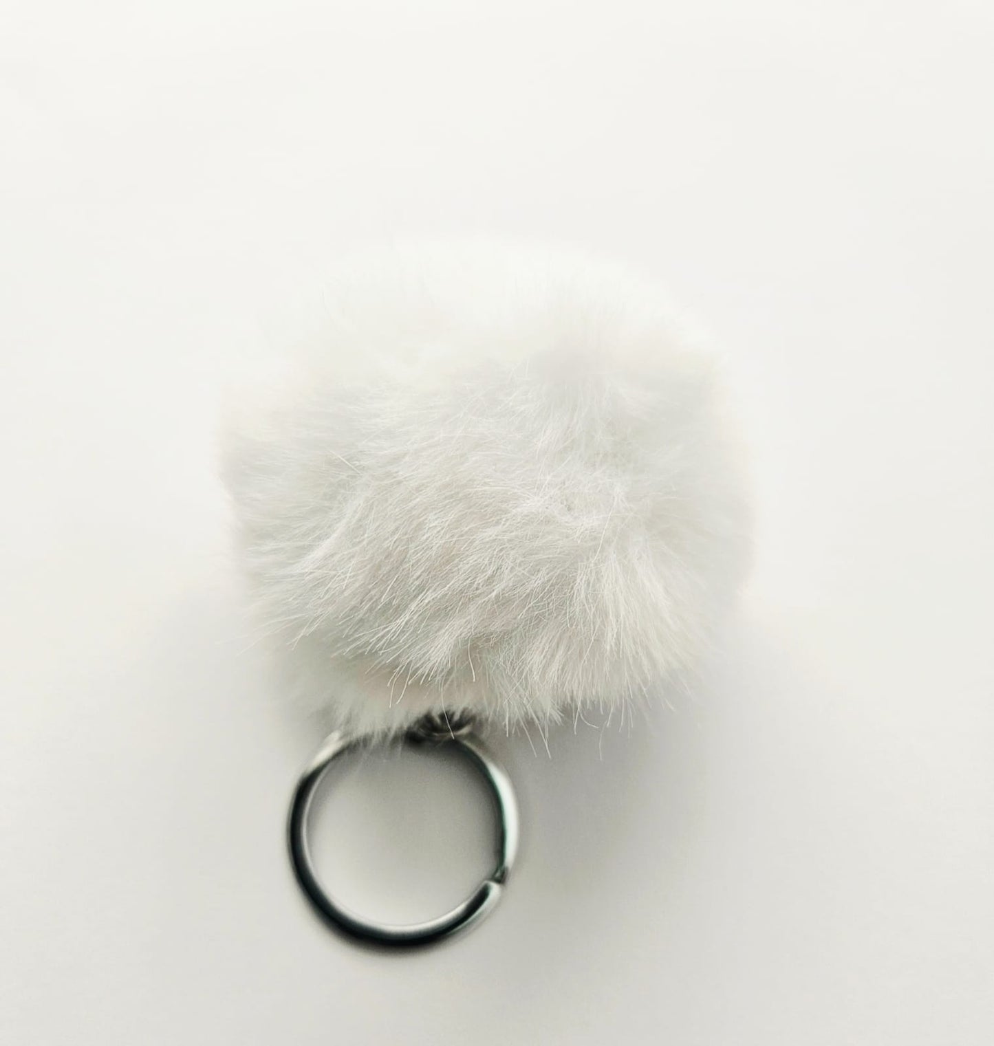 White fluffy pom-pom keychain on a light gray background