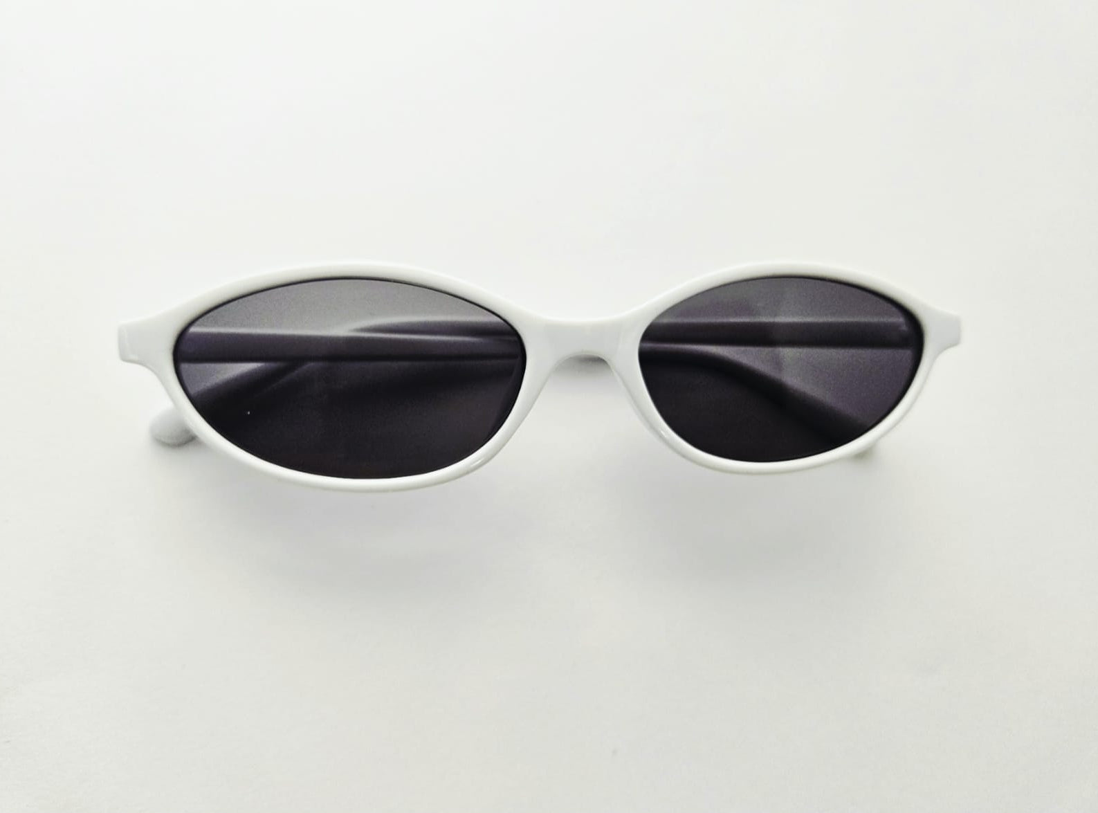 White framed sunglasses with dark lenses on a light gray background