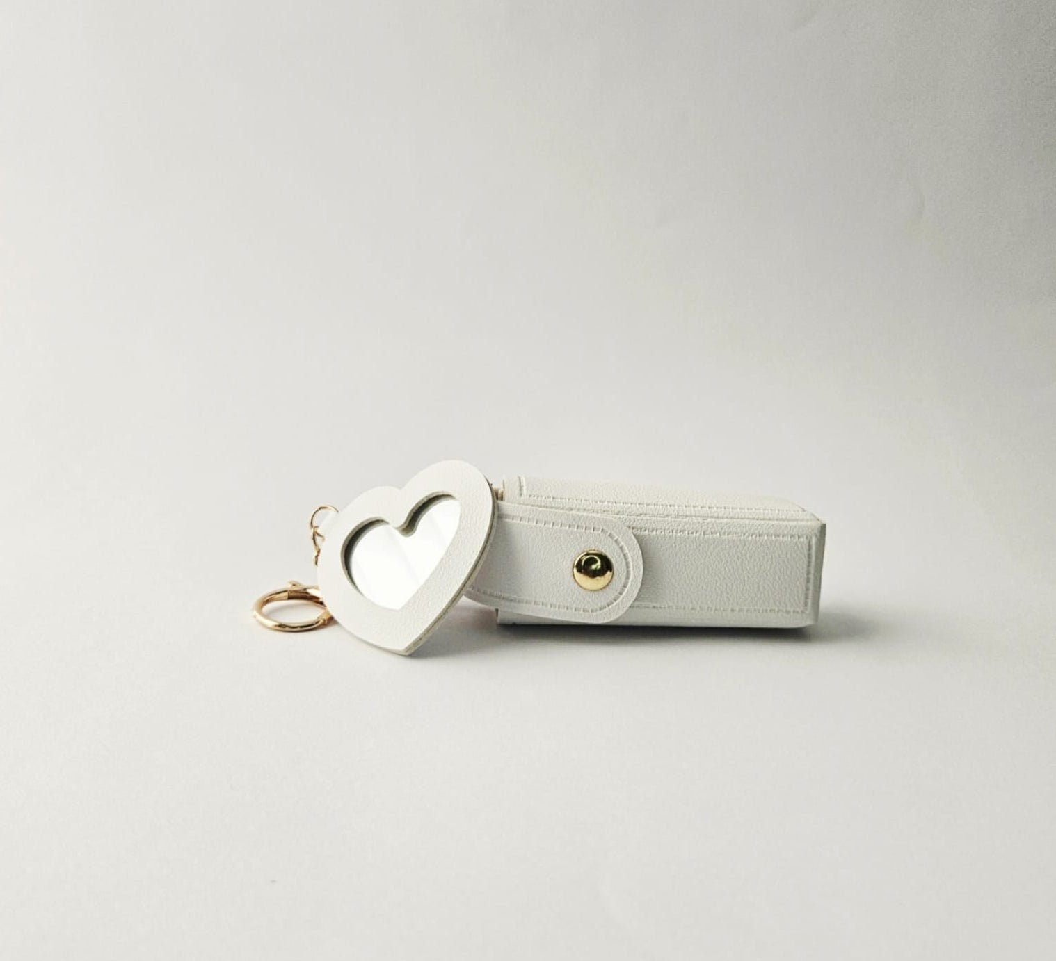 White pouch with heart-shaped mirror keychain on a light gray background