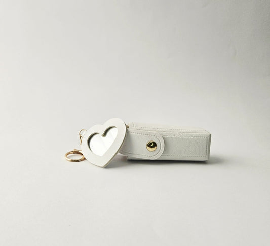White pouch with heart-shaped mirror keychain on a light gray background