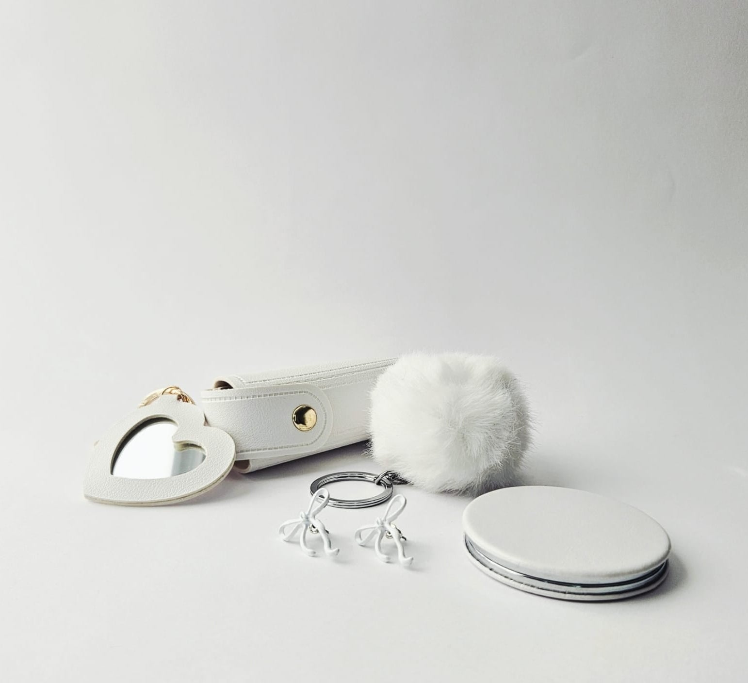 Set of white accessories including a heart-shaped mirror, keychain, and coasters on a light gray background.